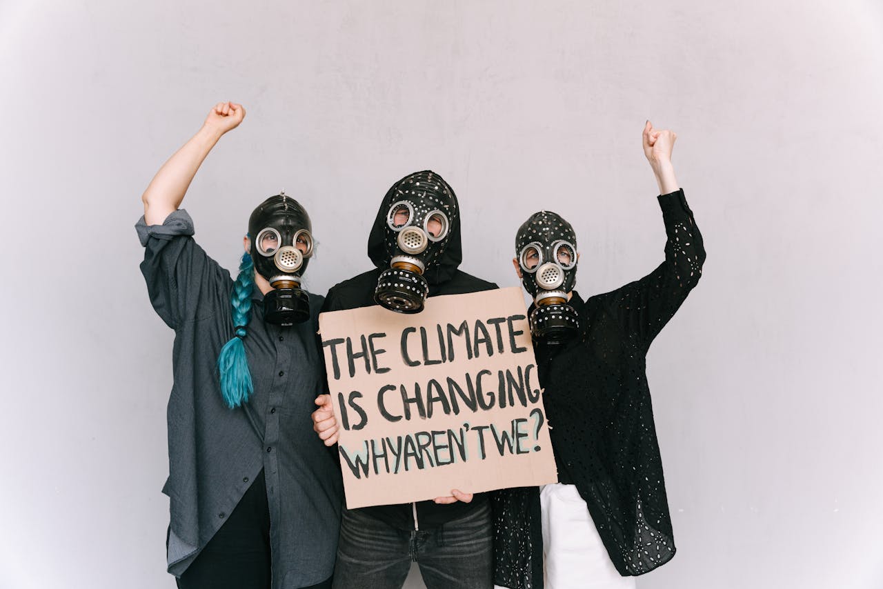 Three activists wearing gas masks hold a climate change protest placard indoors.
